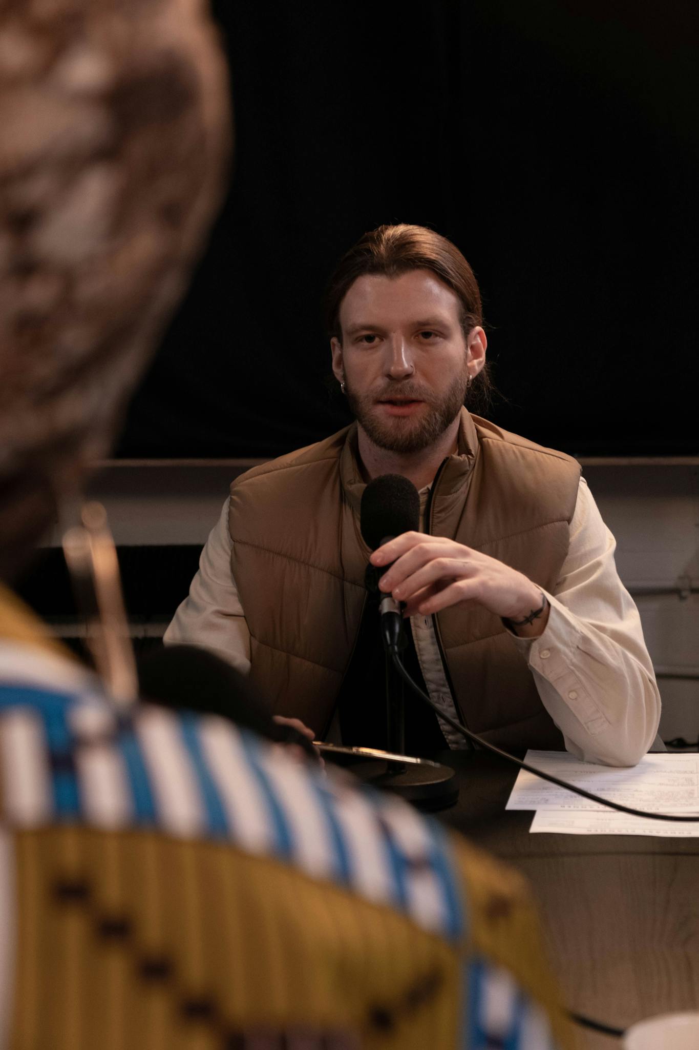 A man holding a microphone conducts an interview in a studio environment.