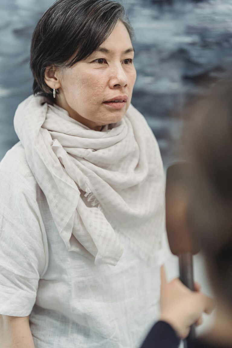 A woman in a light scarf participates in an interview indoors, captured during the day.