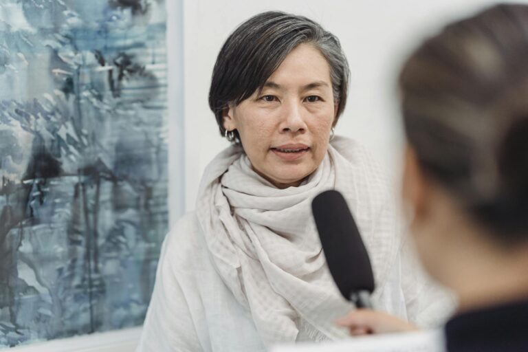 Asian woman in discussion with a journalist at an indoor art gallery.